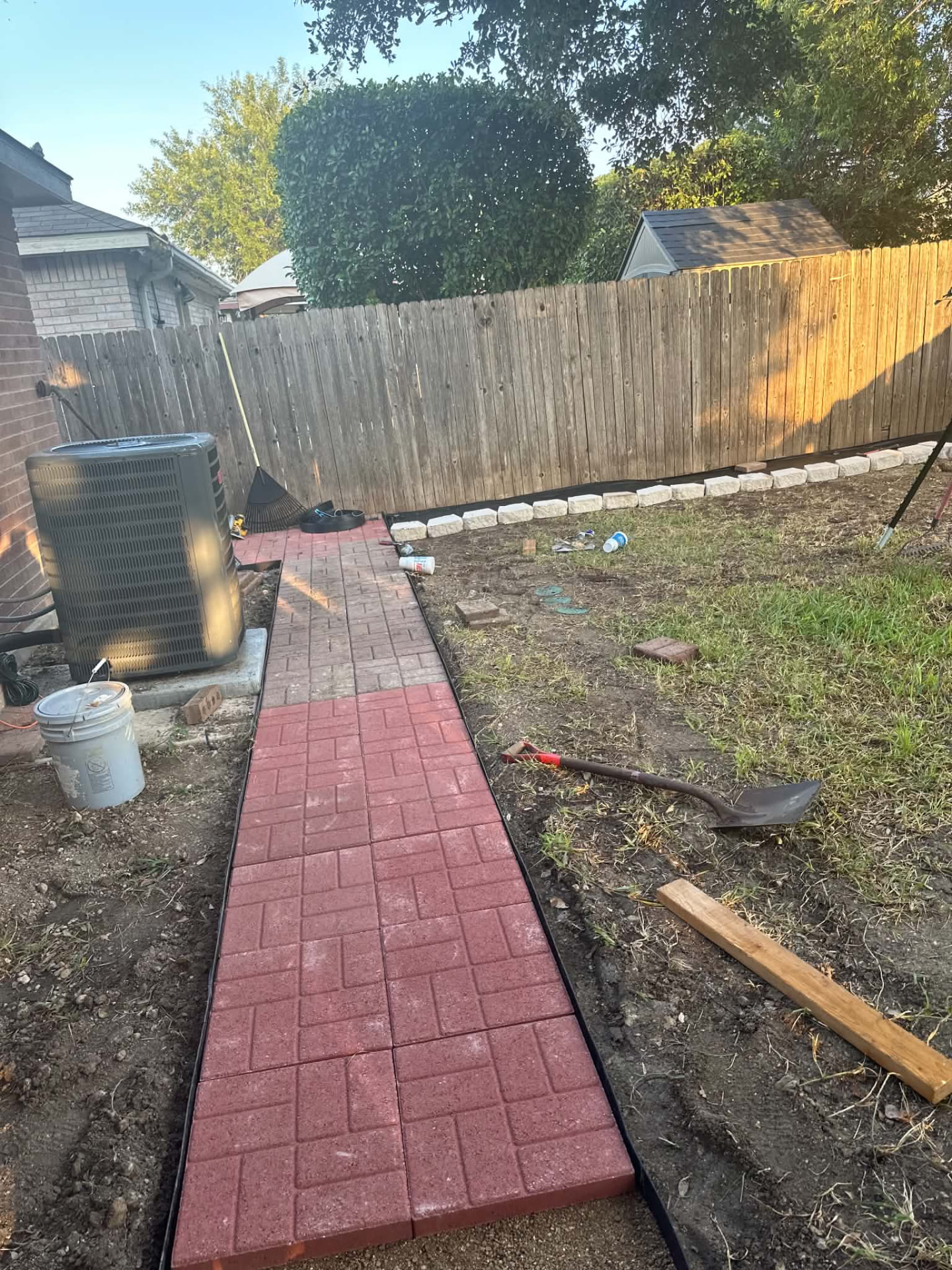 Red paver walkway being installed beside a home and fence