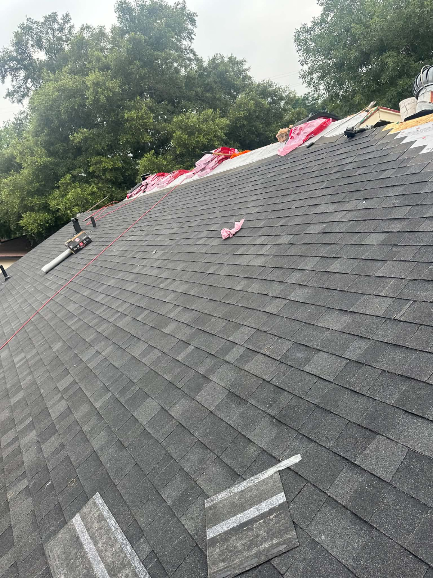 Gray shingles being installed with materials near the roof ridge