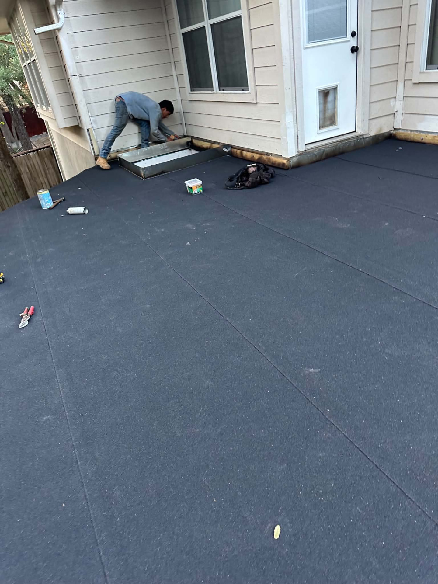 Worker fitting metal detailing beside a house wall and dark surface covering