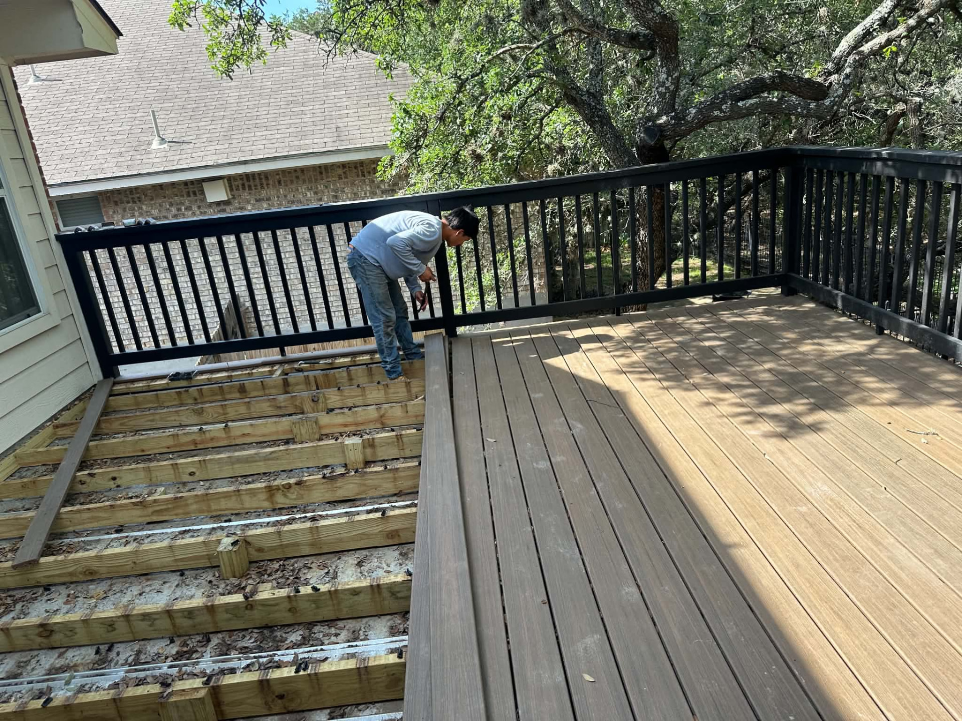 Worker installing deck boards beside exposed framing and black railings