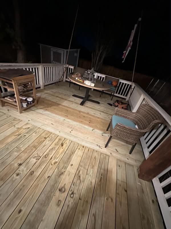 Finished wood deck boards with white railings and outdoor seating at night